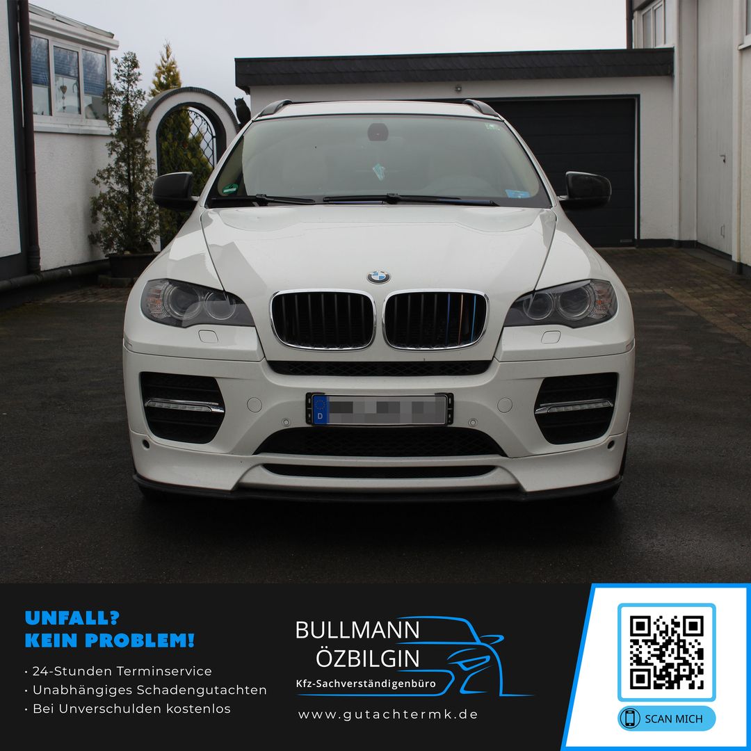 Weiße BMW SUV-Frontansicht mit markantem Kühlergrill und Scheinwerfern, geparkt vor Gebäuden.