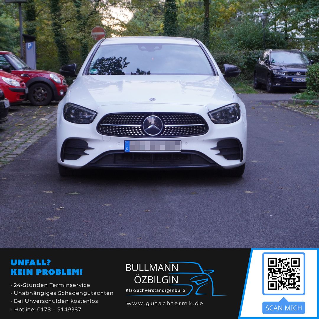 Weiße Mercedes-Benz Limousine frontal auf einer Straße mit parkenden Autos und Bäumen im Hintergrund.