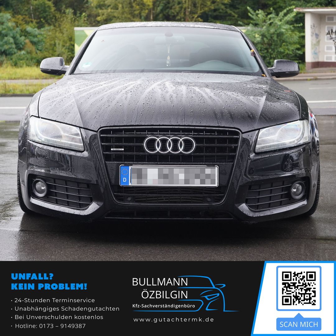 Vorderansicht eines schwarzen Audi-Pkw mit nassen Oberflächen auf einer Straße, umgeben von Grünflächen.