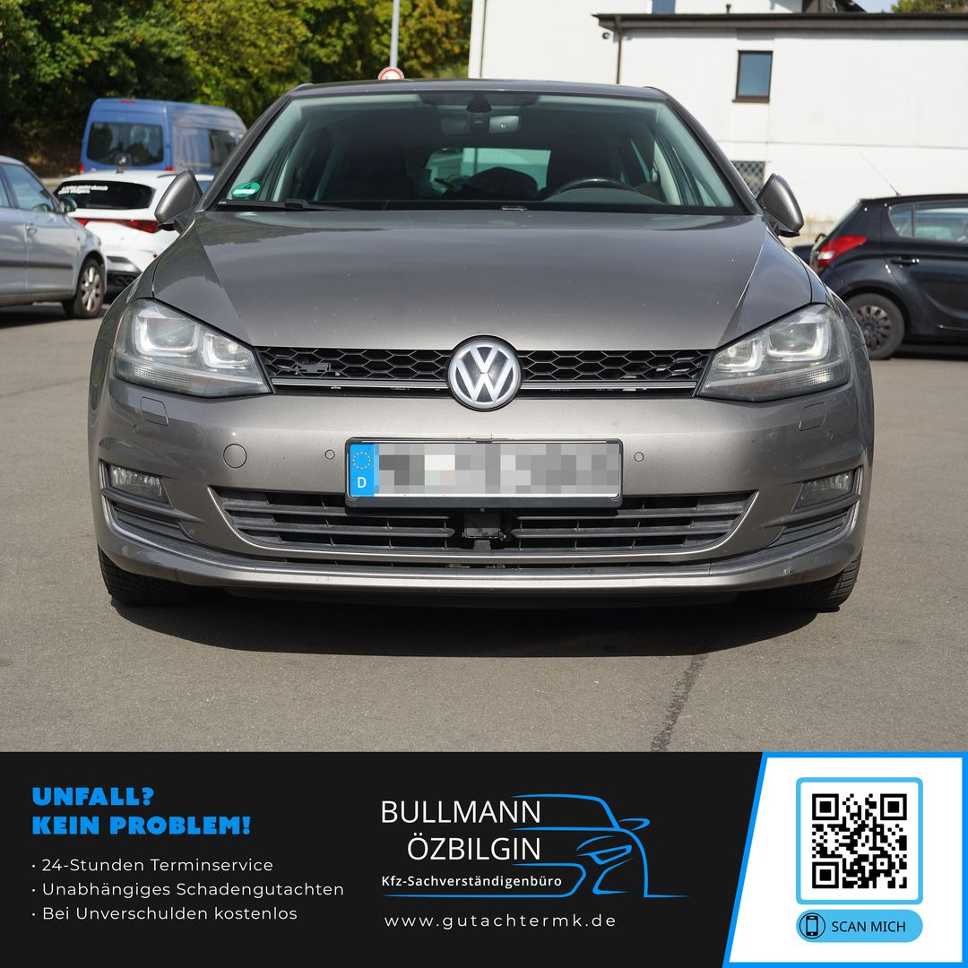 Frontansicht eines grauen Volkswagen Golf, geparkt auf einem Parkplatz mit weiteren Fahrzeugen im Hintergrund.