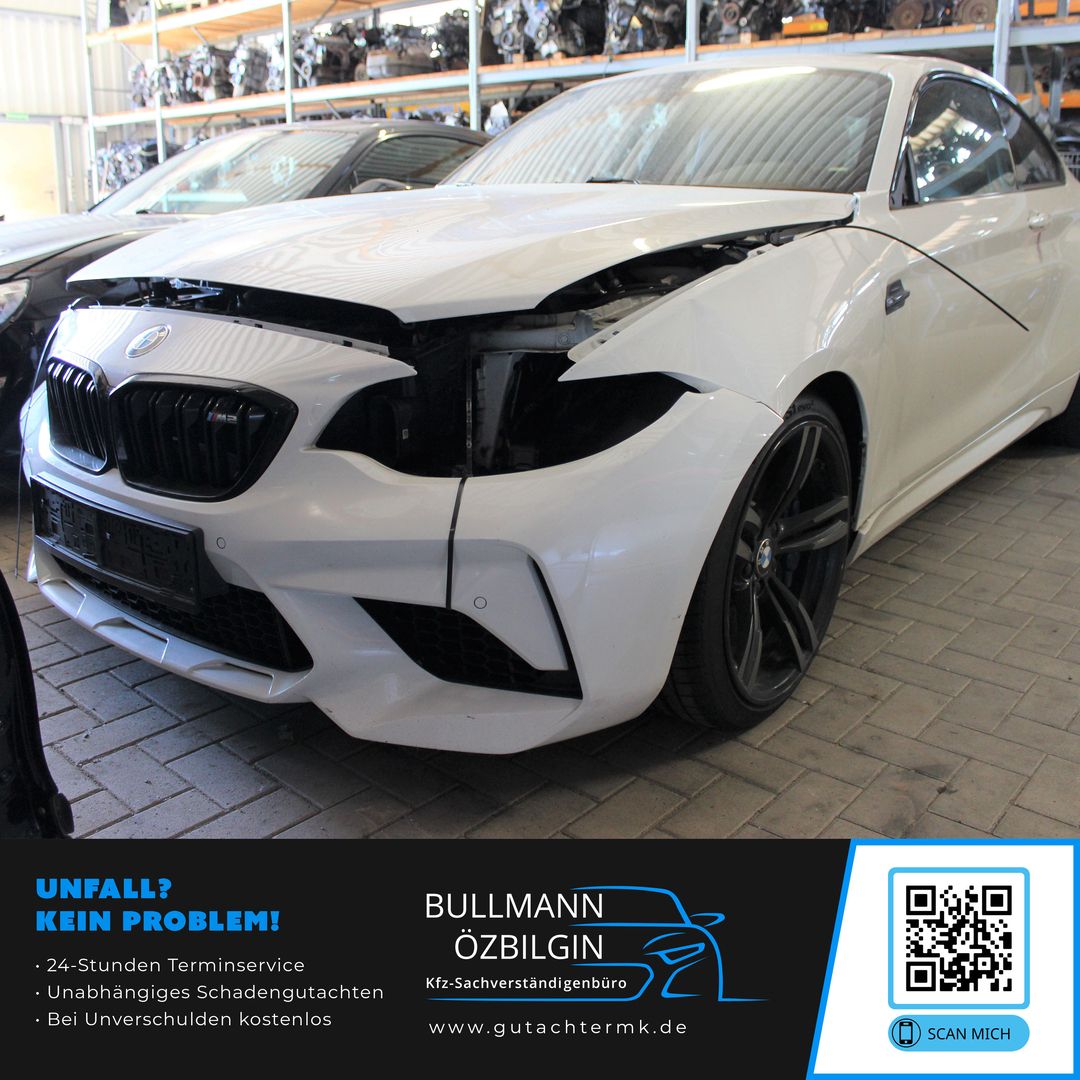 Weißer BMW mit beschädigter Frontpartie, fehlender rechter Scheinwerfer und schwarzer Felge steht in einer Werkstatt.