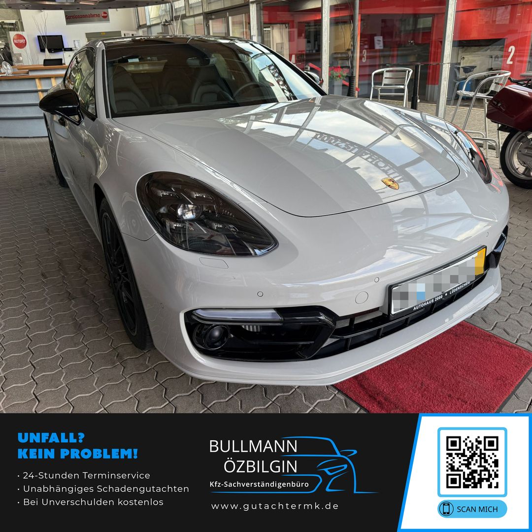 Weißer Porsche Panamera steht in einer Halle auf gepflastertem Boden, Vorderansicht mit sichtbarem Kühlergrill und Scheinwerfern.