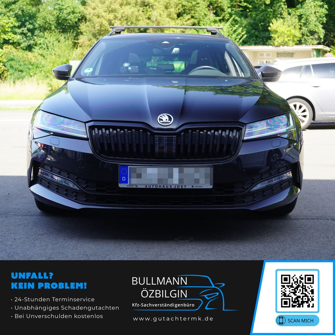 Schwarzes Skoda-Auto von vorne mit sichtbarem Kühlergrill und Logo, parkend auf Asphalt vor grünen Bäumen.