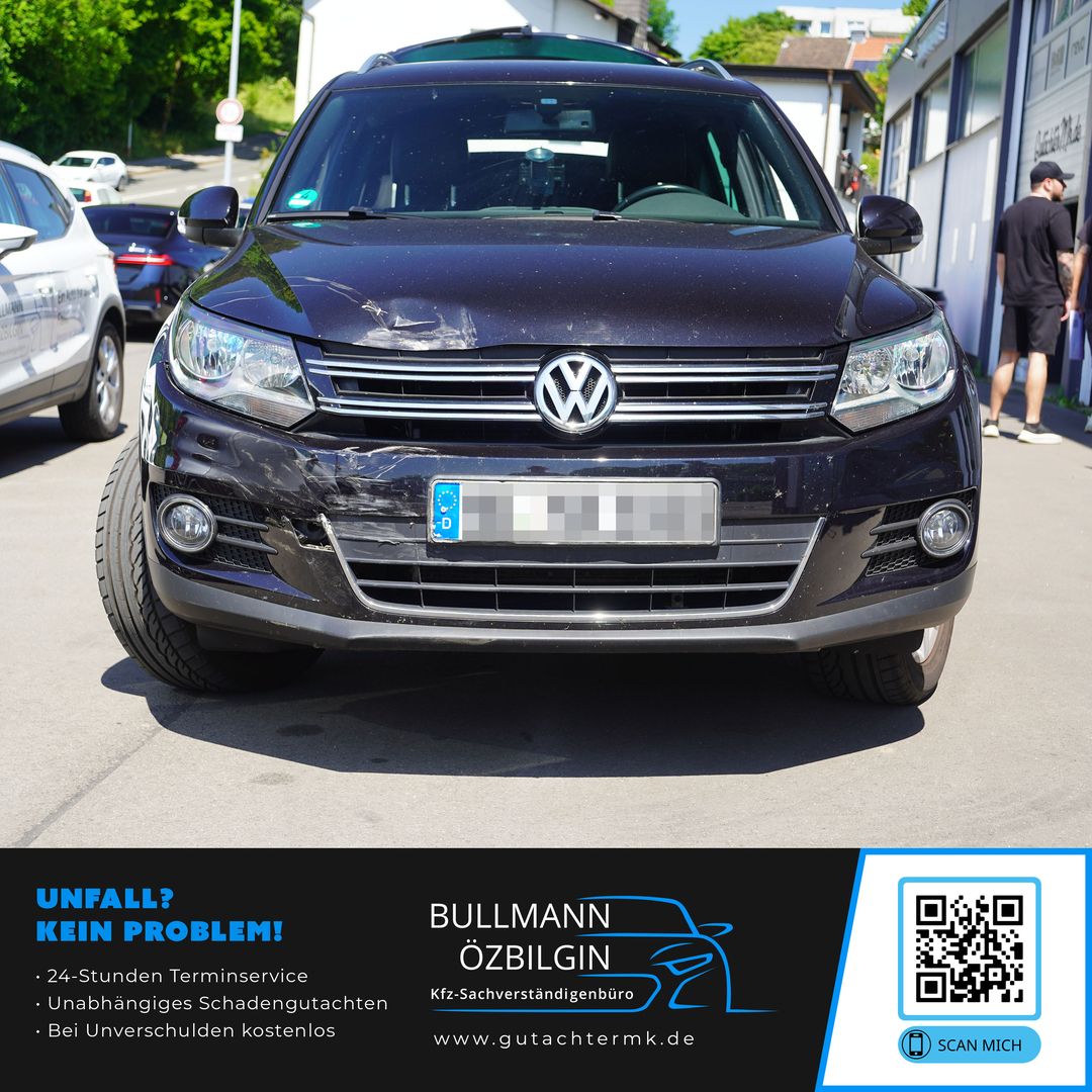 Schwarzer Volkswagen Tiguan mit sichtbaren Kratzern und Dellen an der vorderen Stoßstange, frontal aufgenommen auf einer Straße.